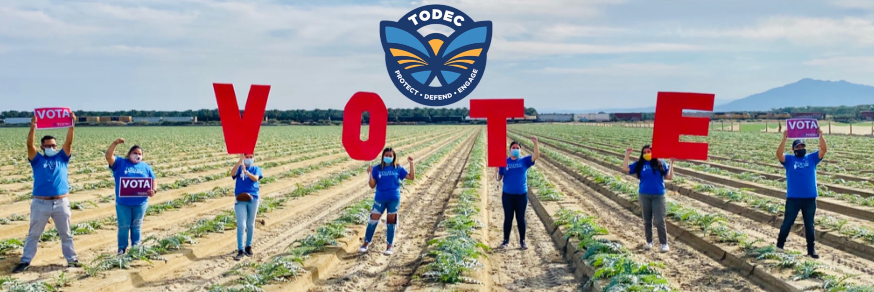 Photo of people standing in an agricultural field holding letters spelling out V-O-T-E